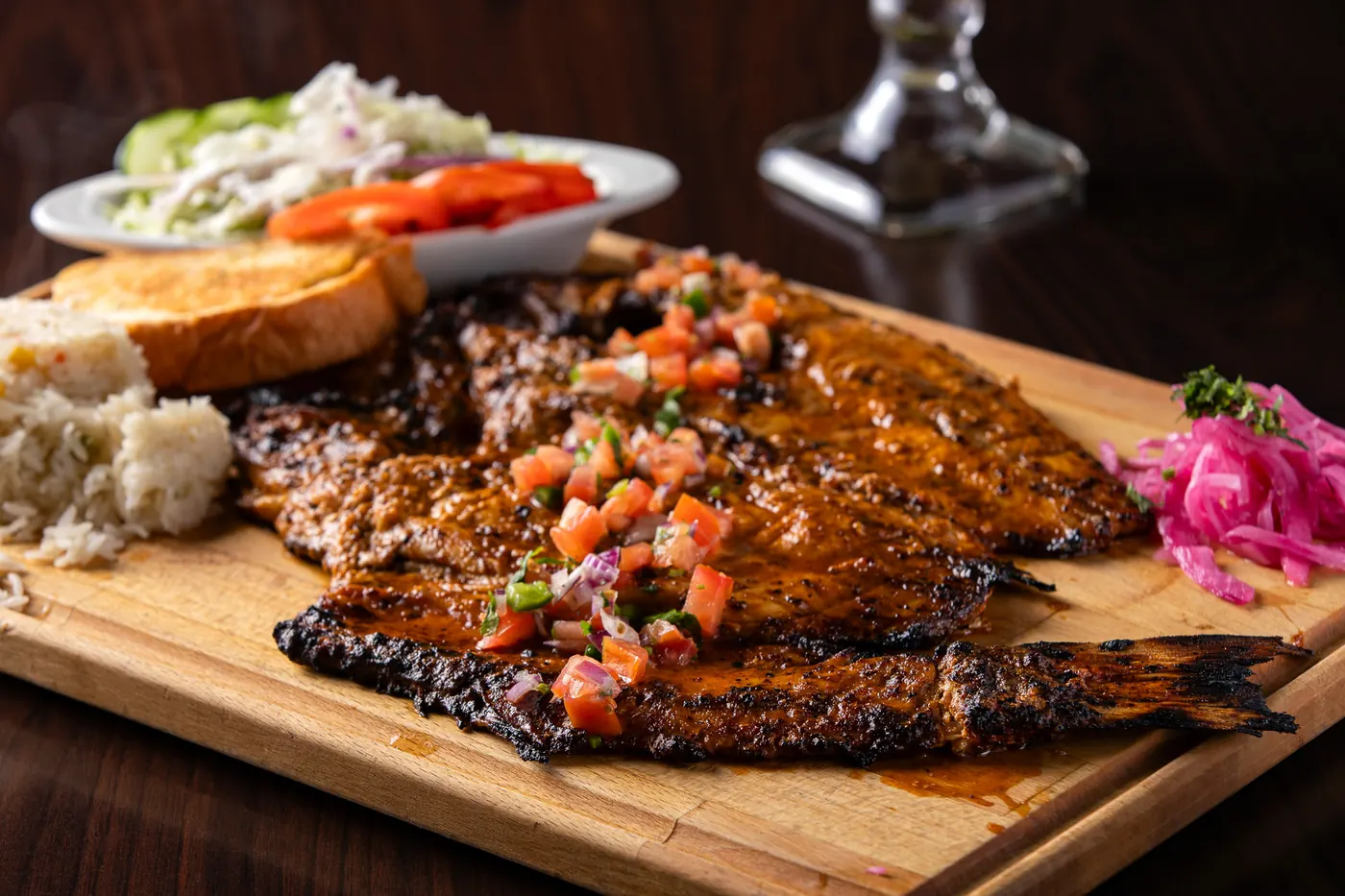 Whole zarandeado-style grilled snapper on a wooden board with pico de gallo